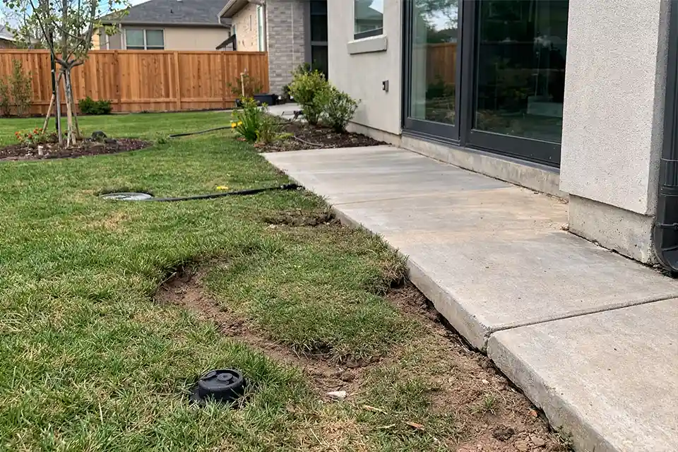 Backyard depression forming next to walkway and foundation due to settling backfill soil.