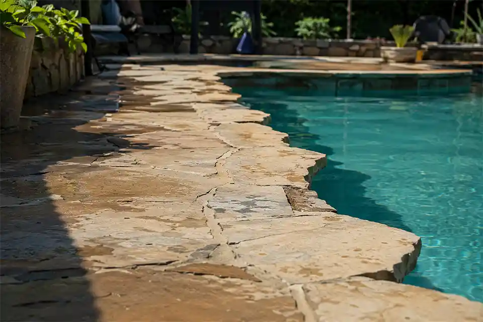 Stone pool deck walking-surface tiles with chipped edges and recessed joints in a high-traffic poolside area