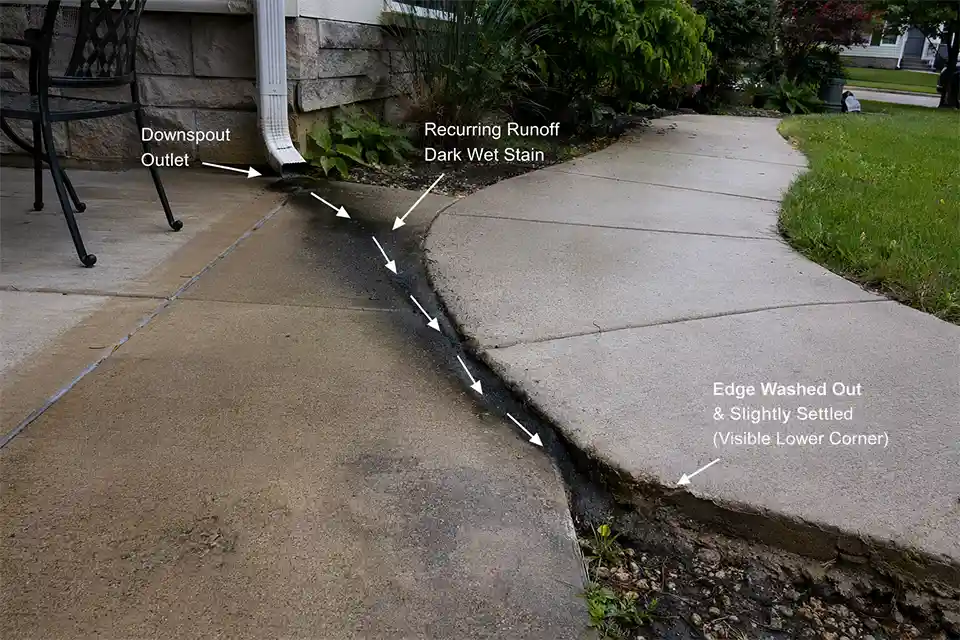 Patio and walkway with a highlighted runoff path causing a dark wet strip, edge washout, and slight settlement